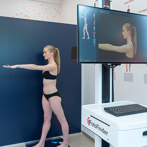 Patientin steht im Untersuchungsraum vor dem ATBM master System zur automatisierten Ganzkörperaufnahme.