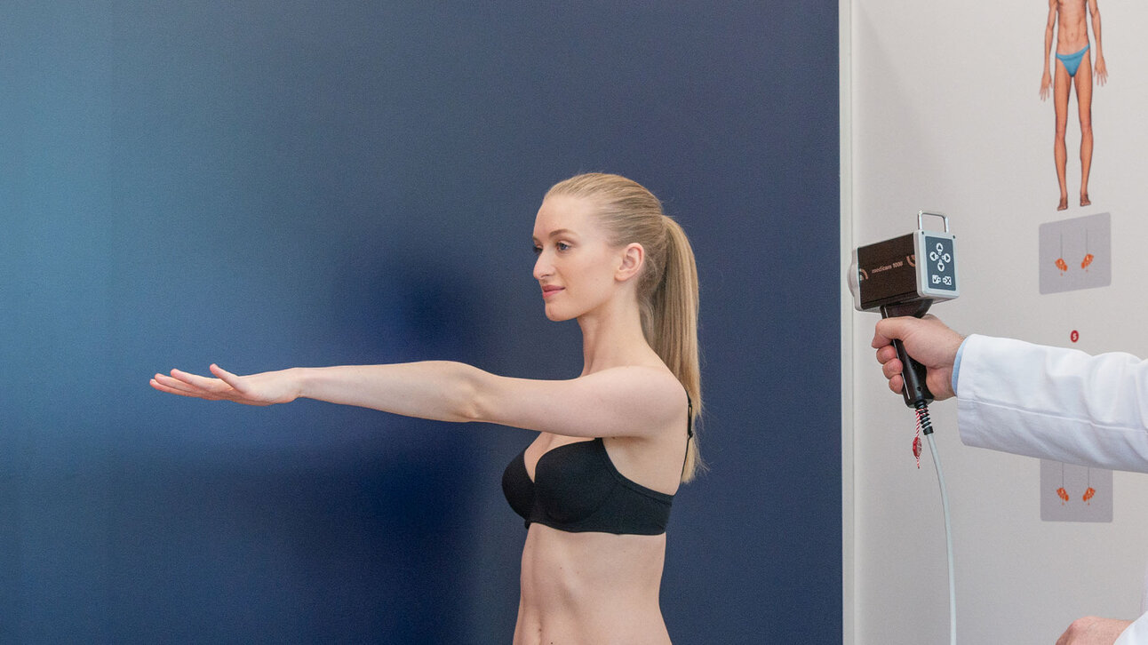 Videodermatoskopische Untersuchung einer Patientin mit ausgestrecktem Arm vor blauem Hintergrund