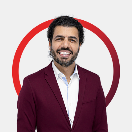 Portrait von Mohadma Daryaie, lächelnd, in einem weinroten Sakko mit weißem Hemd, vor hellem Hintergrund und rotem Kreisrahmen.